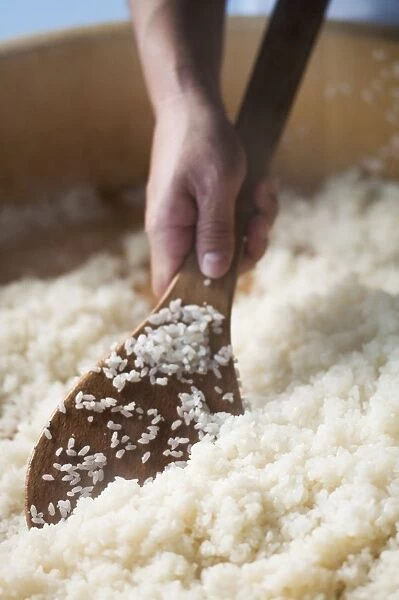 Hand holding wooden spoon in large bowl of white rice, close-up