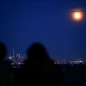 People watch the full moon while it rises over the skyline of New York