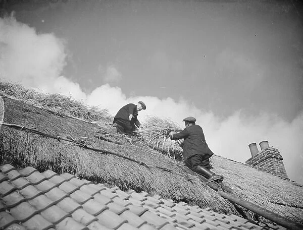 Men work on a tiled roof putting thatching on the roof of a cottage in Orpington