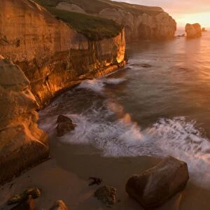 Seascape view down the rugged coastline at Tunnel Beach with sea stacks and rock arches right at sunrise Tunnel Beach, Coastal Otago, South Island, New Zealand