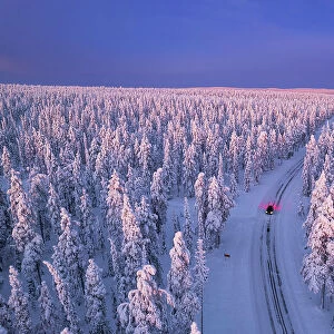 Aerial view of a car driving through the winter forest covered from snow at dawn, Akaslompolo, Kolari, Pallas-Yllastunturi National Park, Lapland region, Finland, Europe
