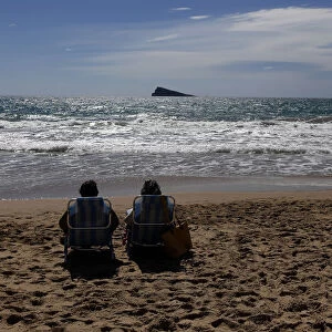 A couple relaxes as they sunbath on a beach during a sunny day in Benidorm