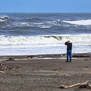 A photographer photographing the waves on the beach at Hokitika in West Coast, New Zealand