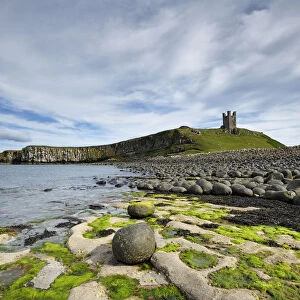 Dunstanburgh Castle on headland of the Whin Sill, eroded dolerite boulders in foreground