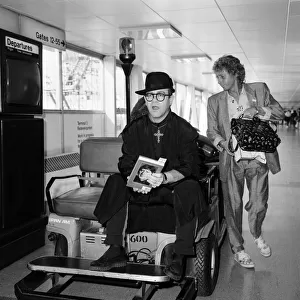 Elton John at Heathrow Airport, wearing a monks black robe and a big gold cross