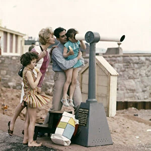 A family at the seaside, loking through a telescope out to sea from the shore